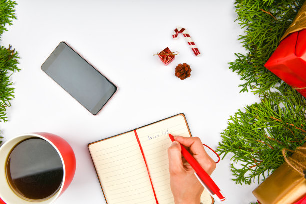 圣诞背景从记事本，电话，咖啡杯。红色陶瓷杯配黑咖啡。新年布局。从上面看。一个女人的手在静脉的笔记本上写字图片下载