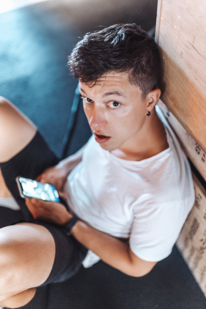 帅哥一边在健身房锻炼一边用手机。图片下载