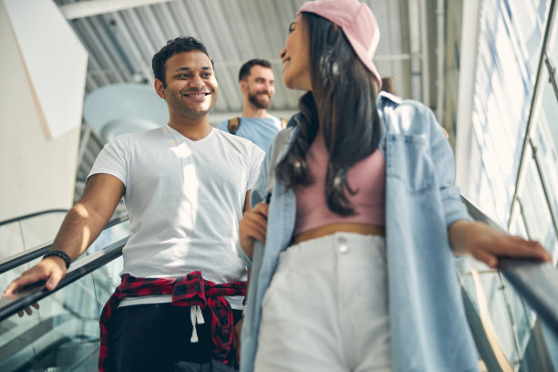 英俊的印度男人站在移动的楼梯上听时髦的女人说话图片下载