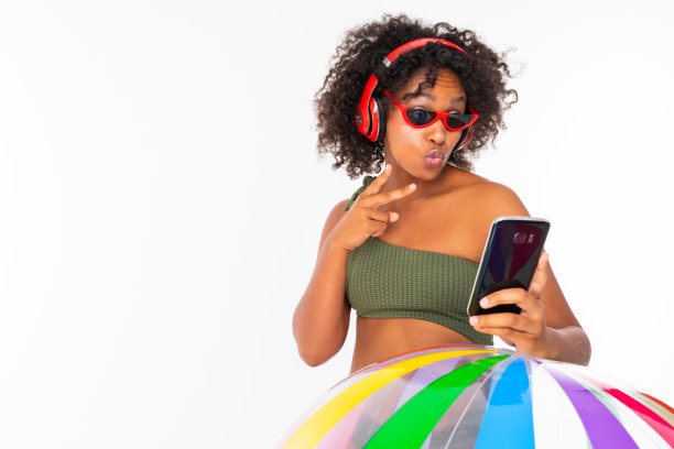 漂亮的非洲女性穿着泳衣站在大彩色橡胶球，听音乐与耳机，做孤立的白色背景自拍图片下载