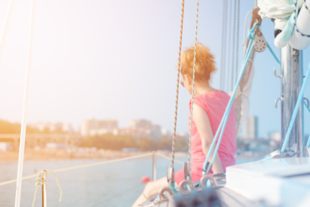 在一个温暖、阳光明媚的夏日，一个女人在游艇上走在海上。图片下载