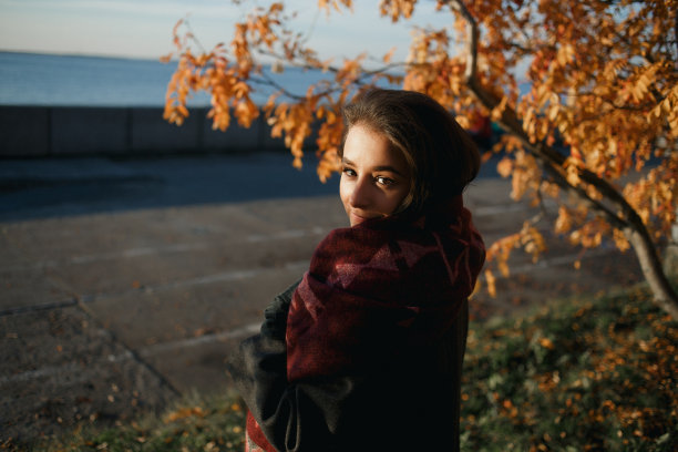户外时尚照片年轻美丽的女士在红色围巾和深灰色外套包围秋天的树叶图片下载