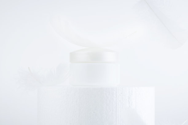空容器白色的化妆瓶放在讲台上，以白色的羽毛为背景。美容或皮肤护理概念。本空间图片下载