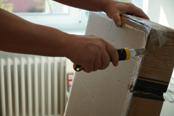 一个男人正在打开一个硬纸板包裹，里面装着家具部件，准备自己组装。特写照片与细节的工作过程，以改善他的家。图片下载