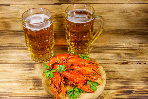 木桌上放着煮小龙虾和两杯啤酒图片下载