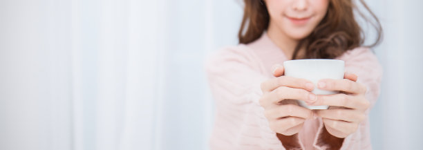 年轻美丽的亚洲女人她的手捧着一杯咖啡，在她的白色卧室冬天的早上时间。快乐愉悦，在寒冷的冬天放松概念横幅图片下载