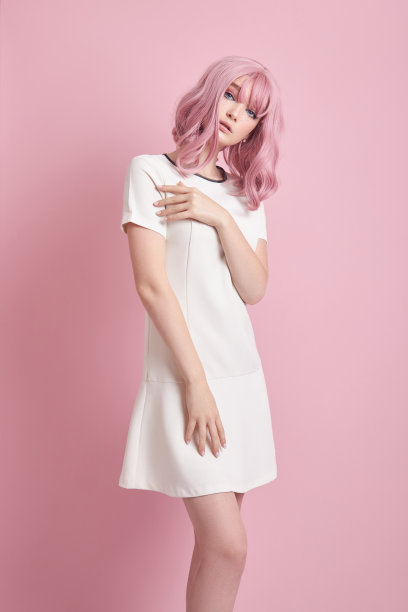 漂亮女孩，粉红头发，染发。可爱的动漫女郎站在粉红色的背景上，穿着白色的短裙。彩色的头发，完美的发型图片下载
