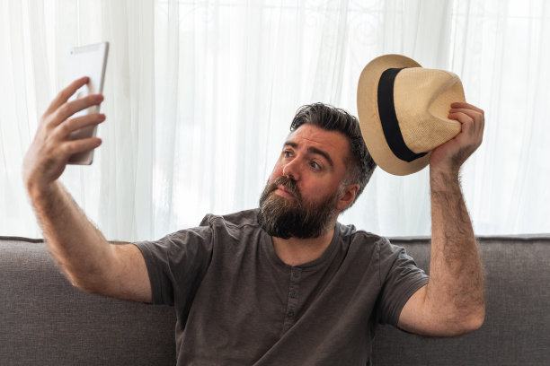 大胡子男人用平板电脑，视频通话，照片，视频会议，坐在沙发上。图片下载