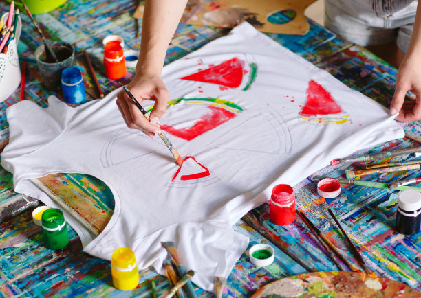 画在衣服上。女孩在一件白色t恤上画画。图片下载