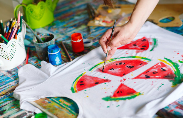 画在衣服上。女孩在一件白色t恤上画画。图片下载