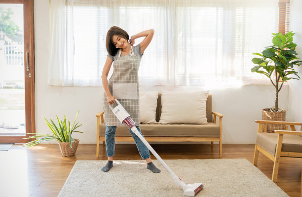 年轻女子家庭主妇在现代客厅用吸尘器打扫地板，整洁少女清洁女佣在家里拿着拖把，家政家政清洁服务理念图片下载