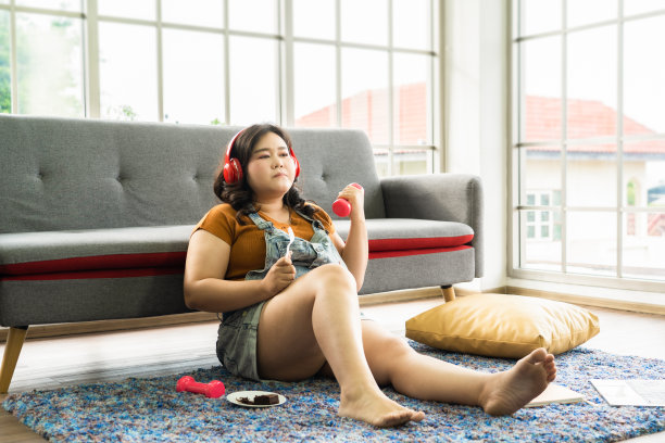 亚洲大码女孩吃锻炼用哑铃和听音乐在家图片下载