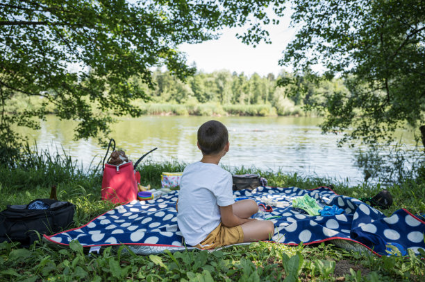 小男孩坐在湖边的野餐毯子上图片下载