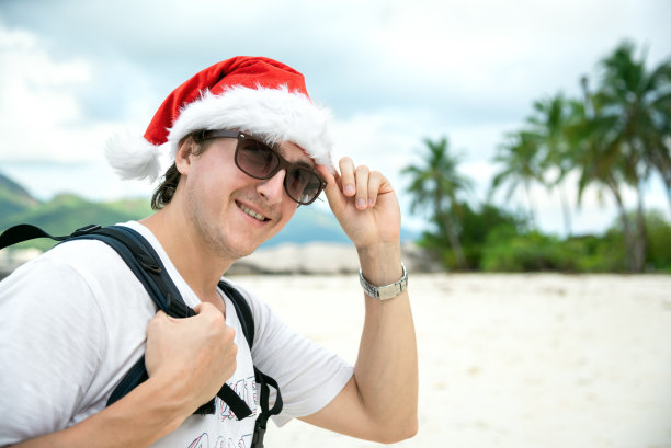 热带海滩上戴着圣诞老人帽和太阳镜的快乐男人。圣诞假期的概念图片下载