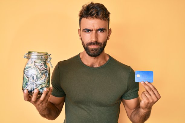 年轻的拉美裔男子持有信用汽车和jar与美元怀疑和紧张，皱眉不安，因为问题。消极的人。图片下载