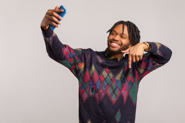 请点赞并订阅。快乐的非洲博主在运动衫做视频在社交媒体上直播，与他的追随者玩得开心。图片下载