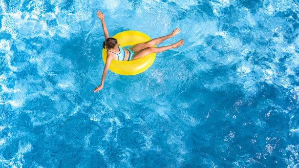 活跃的年轻女孩在游泳池空中俯瞰从上面，孩子放松和游泳在充气圈甜甜圈和在水上有乐趣的家庭度假，热带度假胜地图片下载