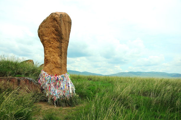 在大草原的高草丛中，矗立着一块底部有许多丝带的古老的高大石头。图片下载