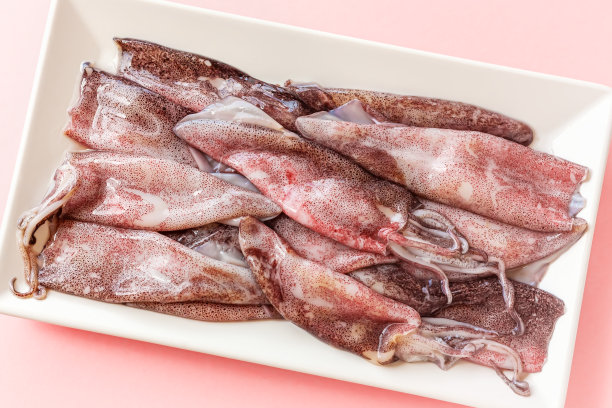 新鲜熟鱿鱼放在白色盘子上，粉红色的背景。前视图。图片下载