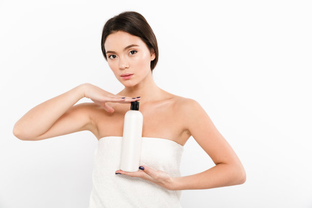 美丽的照片亚洲年轻女子在毛巾拿着瓶子与保湿霜或油在手上，孤立在白色的背景图片下载