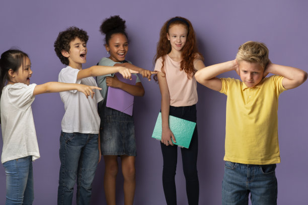 预防欺凌。沮丧的男孩闭上耳朵，而他的同学嘲笑他在淡紫色的背景图片下载