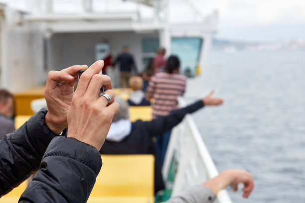 一名男子的手拿着智能手机在渡轮旅行中拍照。背景中其他人模糊的剪影。图片下载