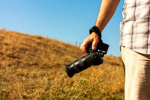 一个男人拿着相机站在山上，黄色的草被太阳晒干了。旅行和国际摄影日的概念。图片下载