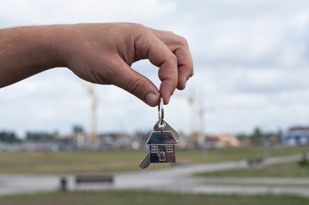 在公寓建筑的背景下，盖伊手里拿着房子的钥匙。关于购买新房的概念。图片下载