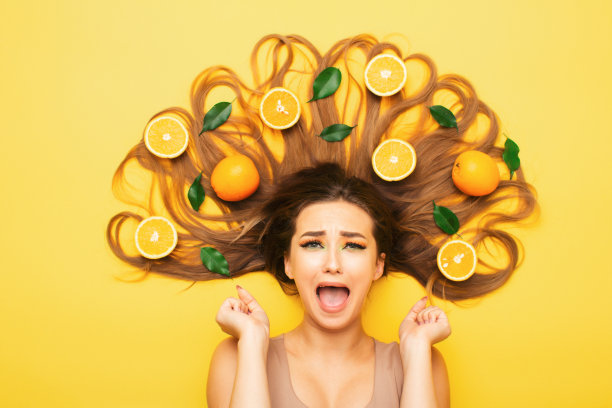 女孩躺在橘子水果在长发绝望的尖叫，年轻的震惊女人与柑橘片和树叶，情绪飞溅图片下载