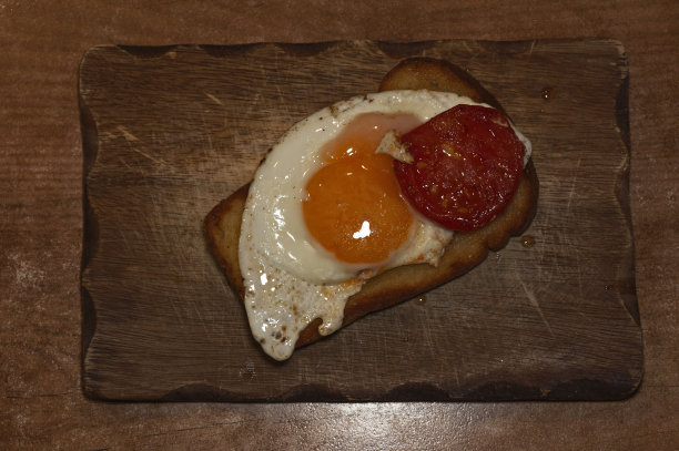 这是一张用黄油煎过的西红柿片煎鸡蛋，放在烤面包片和一块木板上的艺术照片图片下载