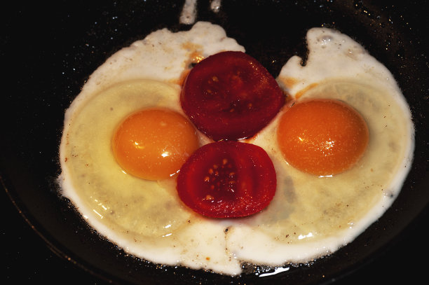 这是在黑色煎锅里用黄油煎西红柿片和煎蛋的艺术照片图片下载