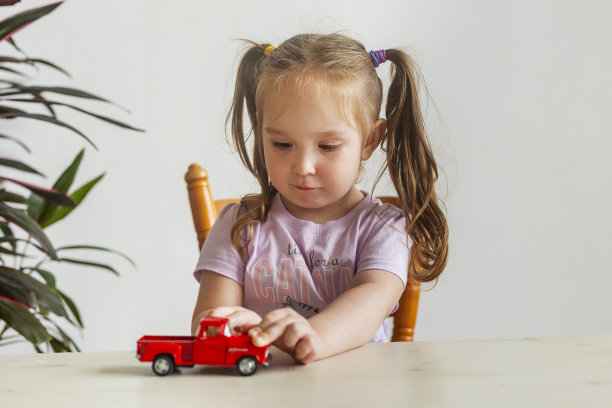 可爱的小女孩在玩红色的小玩具车。图片下载