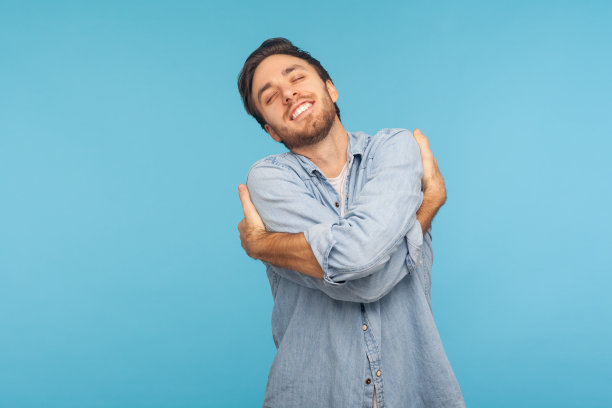 我爱我自己!自私自利的男人的肖像，穿着工人牛仔衬衫拥抱自己，微笑，蓝色背景图片下载