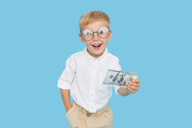孩子和金钱。戴着眼镜、穿着白衬衫的聪明男孩拿着一张蓝色背景的纸币。儿童教育受益贷款的概念。图片下载