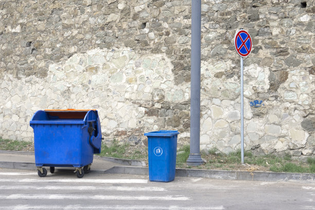 蓝色的塑料垃圾桶和石头墙背景下的路标。图片下载
