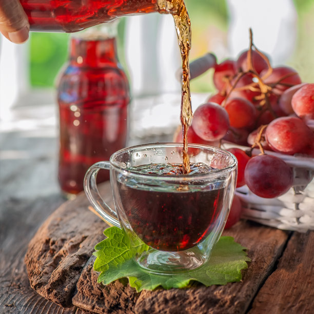 葡萄汁从瓶子里倒进玻璃杯里。白柳条篮子里的一串葡萄。葡萄汁在一个透明的瓶子里图片下载