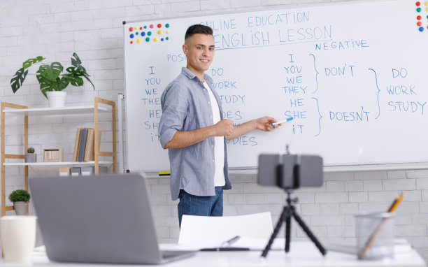 在线导师远程。年轻人微笑着指着白板，看着摄像头图片下载