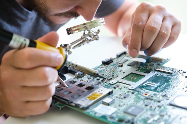 年轻人通过放大镜用烙铁修理印刷电路板图片下载