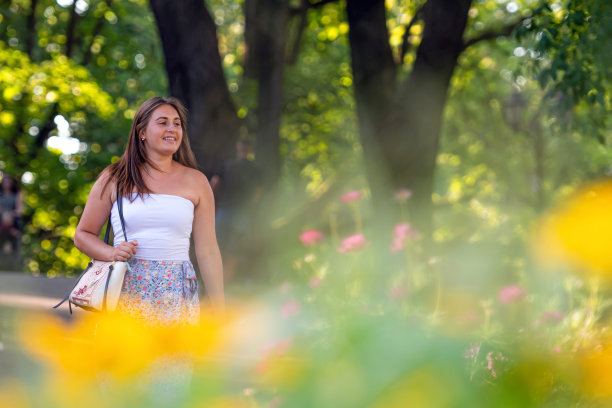 一个穿着浅色上衣和杂色裙子的年轻女子走过城市公园图片下载