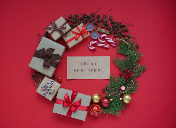 圣诞花环制作的礼盒，圣诞树枝，松果，圣诞玩具球，蜡烛，棒棒糖和肉桂与文字圣诞红色背景俯视图。圣诞贺卡的概念图片下载