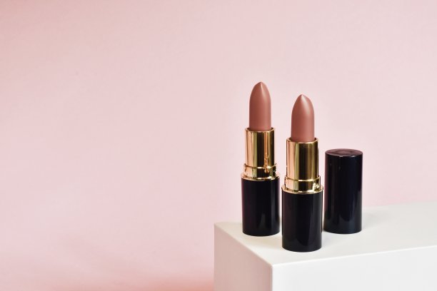 粉色哑光口红控股在一个白色的立场上粉红色的背景。 美容行业产品概念。迷人的化妆配件近距离粉红色。美容、典雅的属性。副本的空间。图片下载