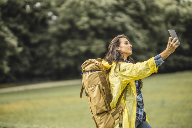 穿着黄色雨衣的年轻女子用智能手机自拍，微笑着享受和休息在自然中图片下载