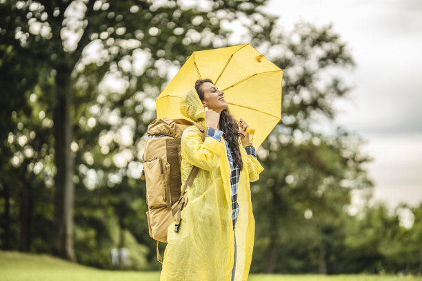 女性美丽的年轻游客拿着黄色的雨伞，穿着黄色的雨衣，享受着大自然图片下载