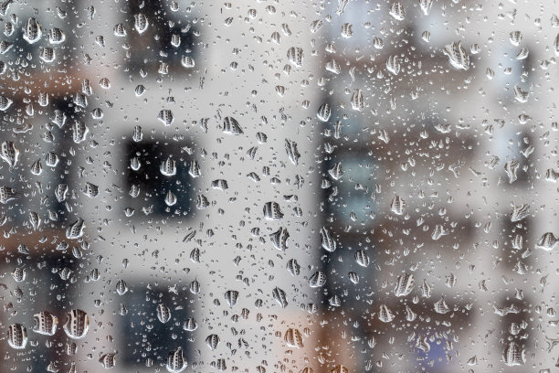 在阴雨霏霏的日子里，一间房子模糊的背景下，水滴落在窗户玻璃上。不同大小的雨滴反映了附近的公寓楼图片下载