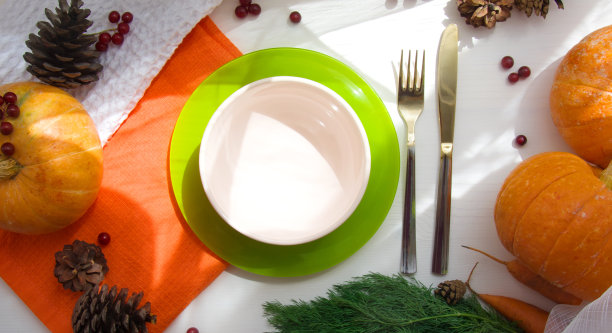 白色的木制餐桌上放着南瓜、胡萝卜、欧芹和蛋卷，旁边放着橙色的餐巾，阳光下放着一个空盘子。秋天的收获。万圣节。从以上观点。图片下载