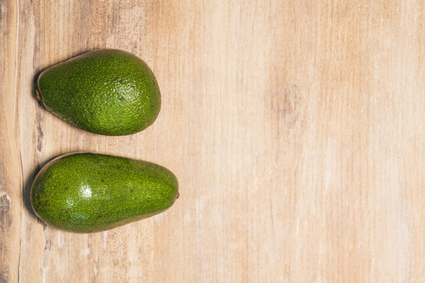 两个新鲜的绿色鳄梨放在一张木桌上，俯视图。为你的文本复制空间图片下载