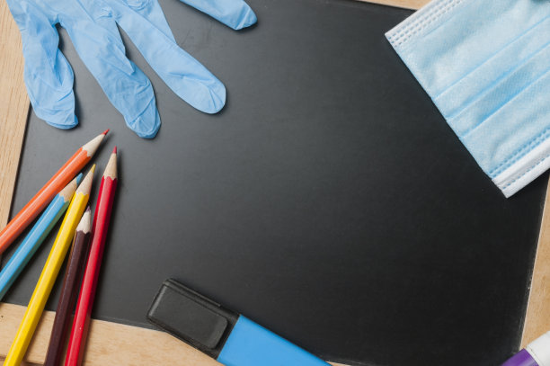 在covid-19大流行期间返回学校的概念:一块装有一些学校物品的黑板，一个外科口罩和防护手套图片下载