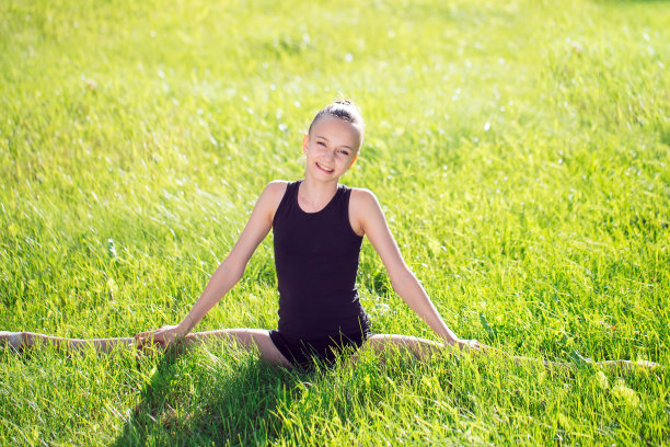 一个阳光明媚的日子，美丽的小女孩在草地上做体操。图片下载