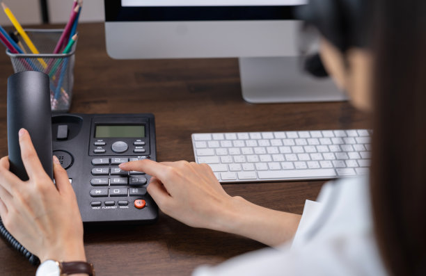 在办公桌上拿着电话和工作笔记本电脑的女人。图片下载