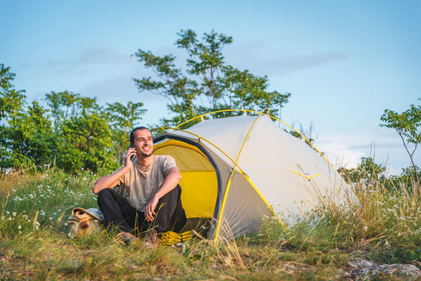 一个年轻的白人在帐篷外打电话。户外露营休闲活动概念。图片下载